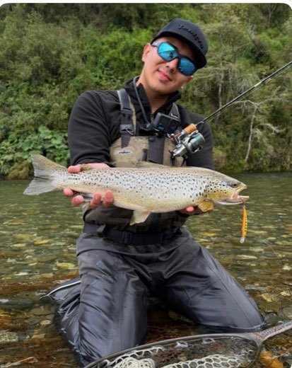 Sebastián Méndez sosteniendo una trucha marrón en un río